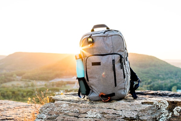 Digital nomad backpack standing on a rock with a mountain and the sunset in the back.