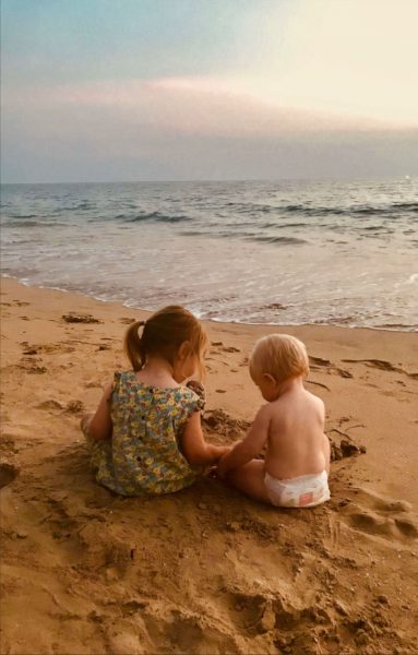 Two small kids sitting at the beach.