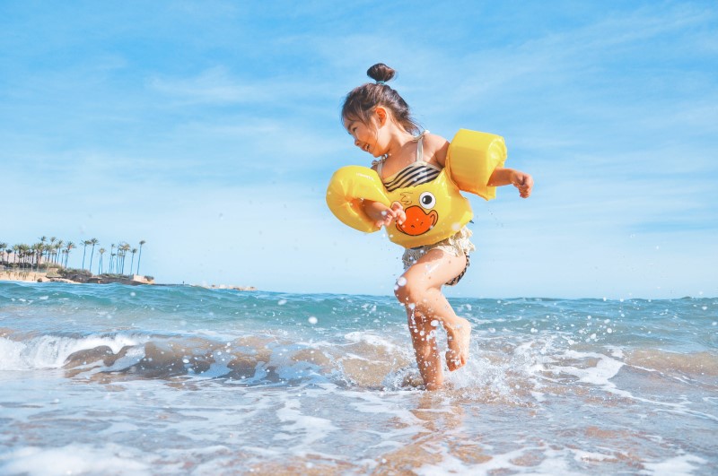 A little girl is jumping in the water of the ocean wearing floaties.