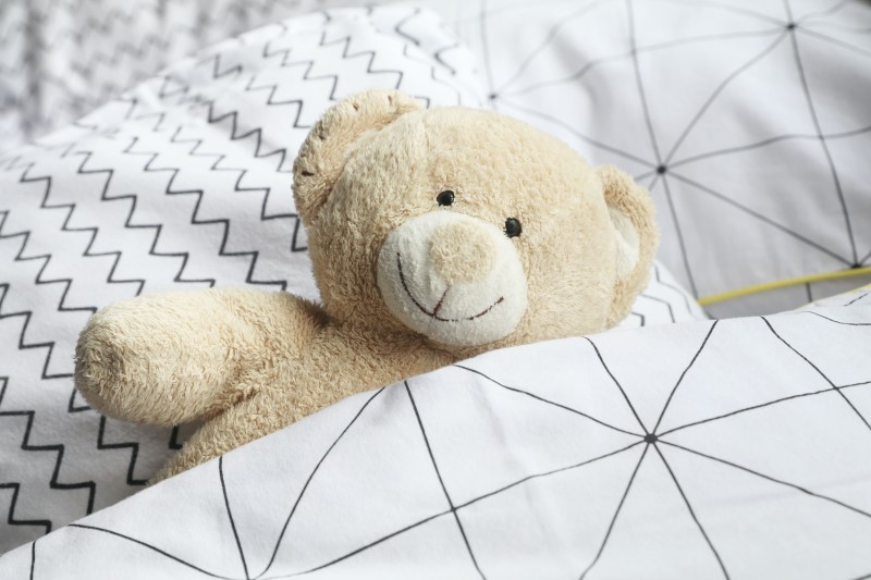A stuffed teddy bear partially covered with a blanket - for the complete toddler packing list.